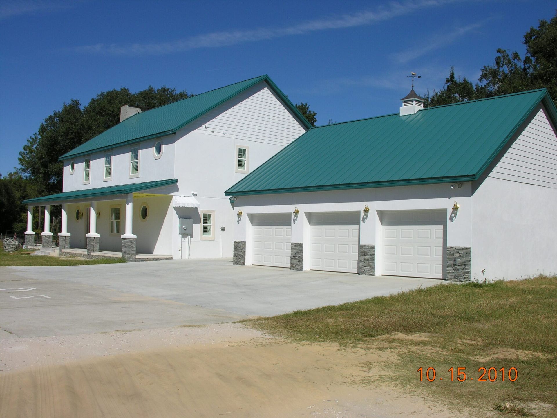 White house with a teal roof and three-car garage. The house has a porch with columns.
