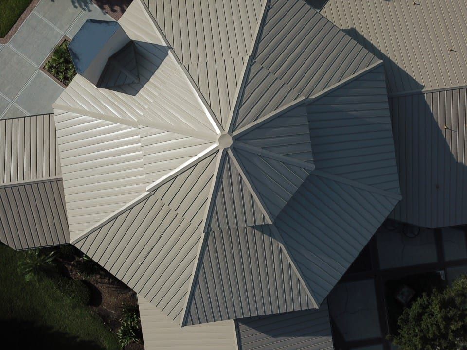 Overhead view of a geometrically shaped roof with a metallic finish. The roof is centered and surrounded by other structures.