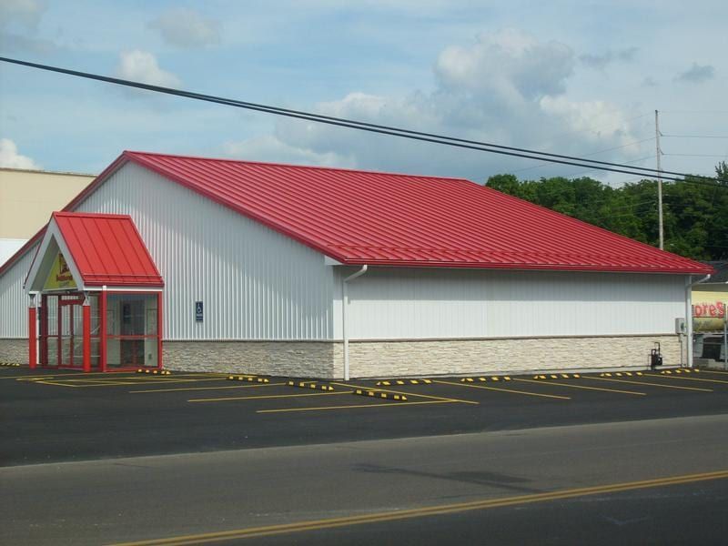 White commercial building with a red roof and entrance, and a paved parking area.