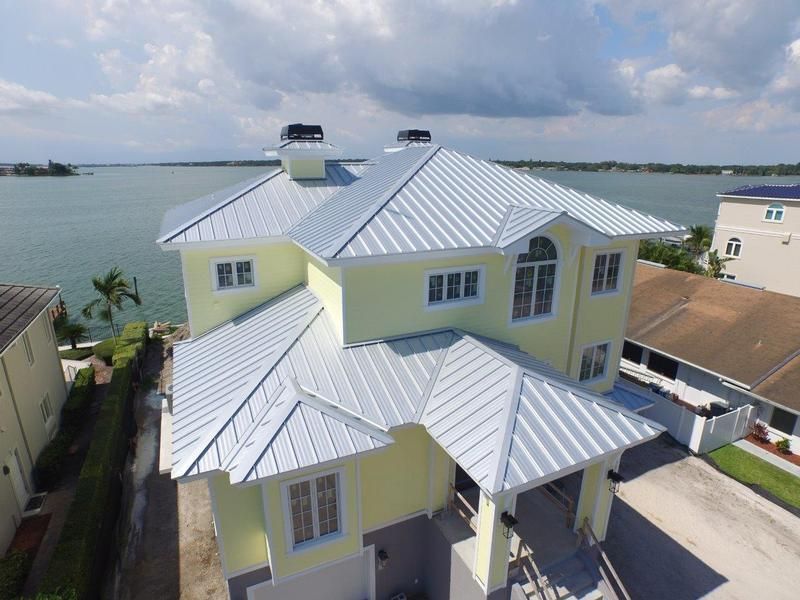 Yellow house with silver metal roof overlooking water on a sunny day.