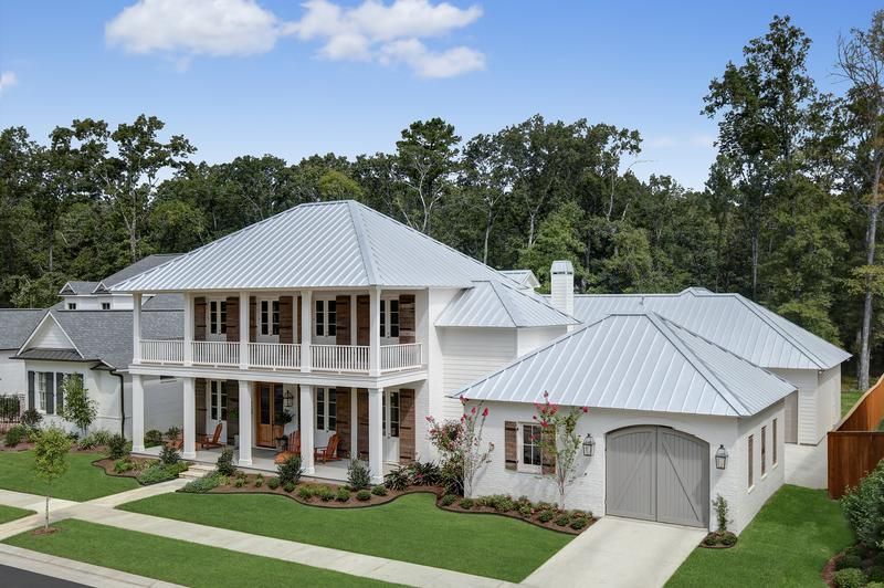Two-story white house with a gray metal roof, wooden shutters, and a green lawn.