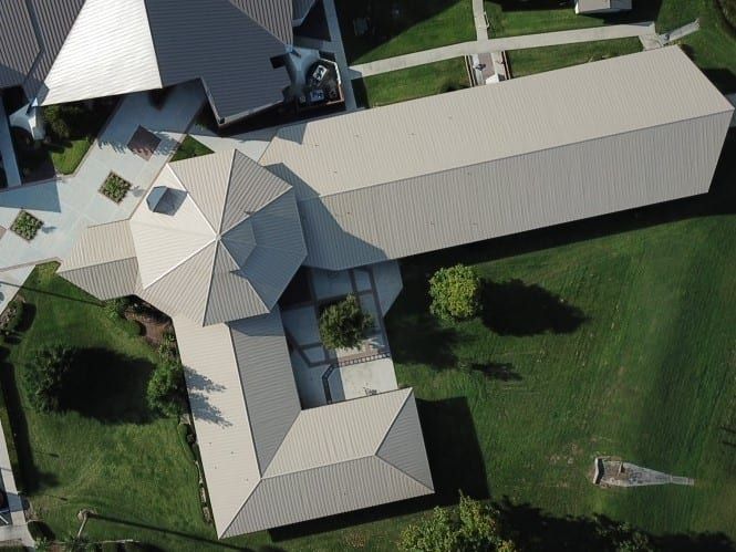Aerial view of building with light-colored metal roof, surrounded by green grass and landscaping.