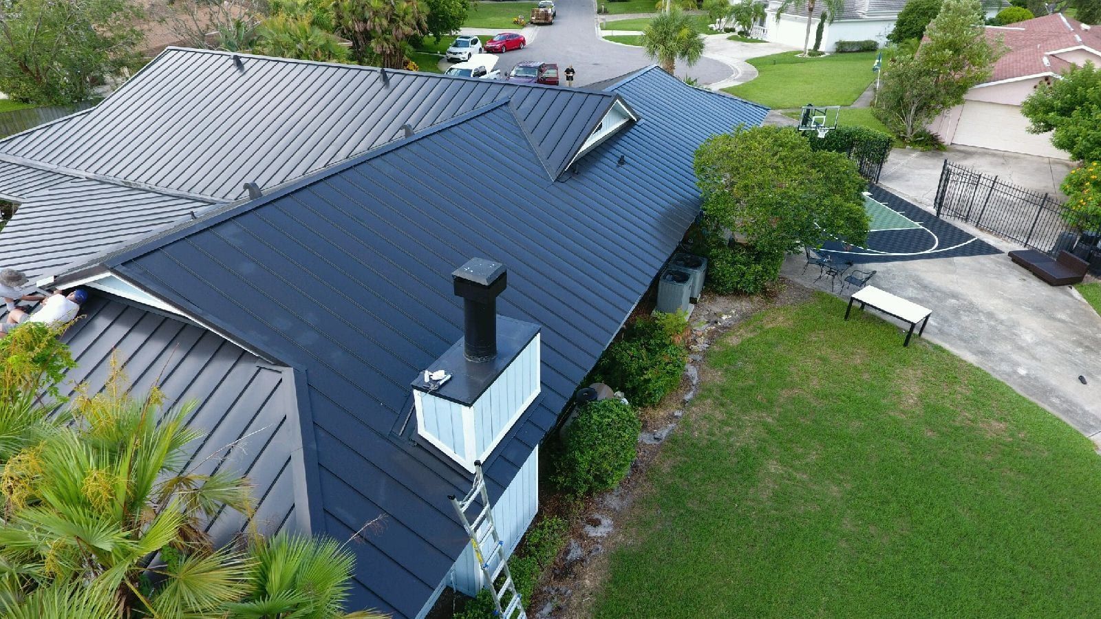 Black metal roof on a house, green lawn, chimney, palm tree, sunny day.
