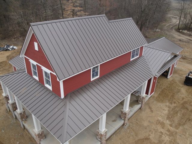 Red house with gray metal roof and white trim. Porch with pillars.
