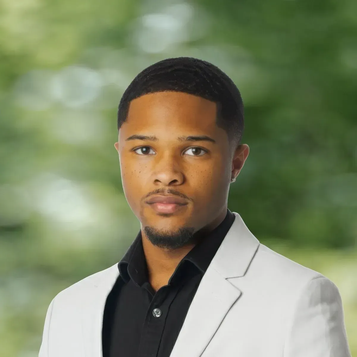 Portrait of a man in a light gray blazer and black shirt against a blurred green background