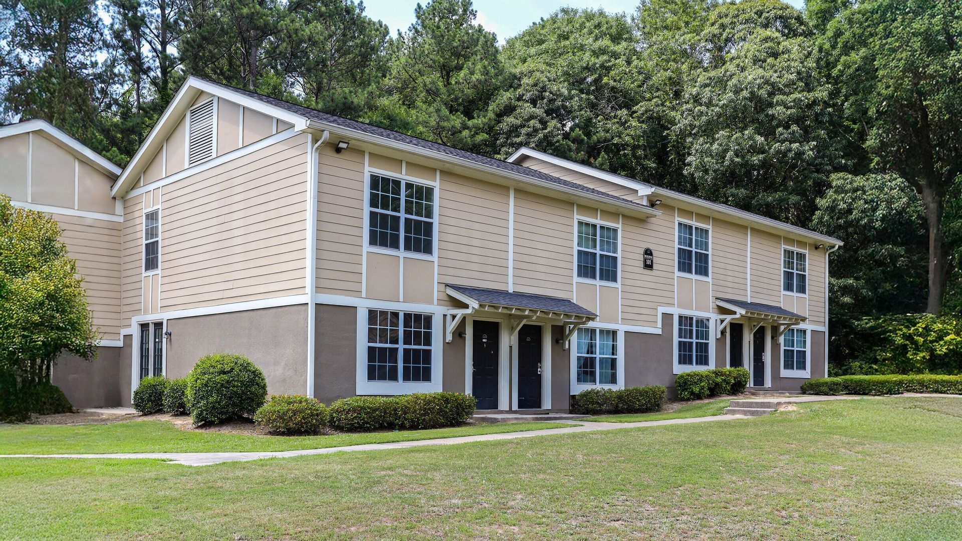 Two-story beige apartment building with white trim, surrounded by green lawn and trees