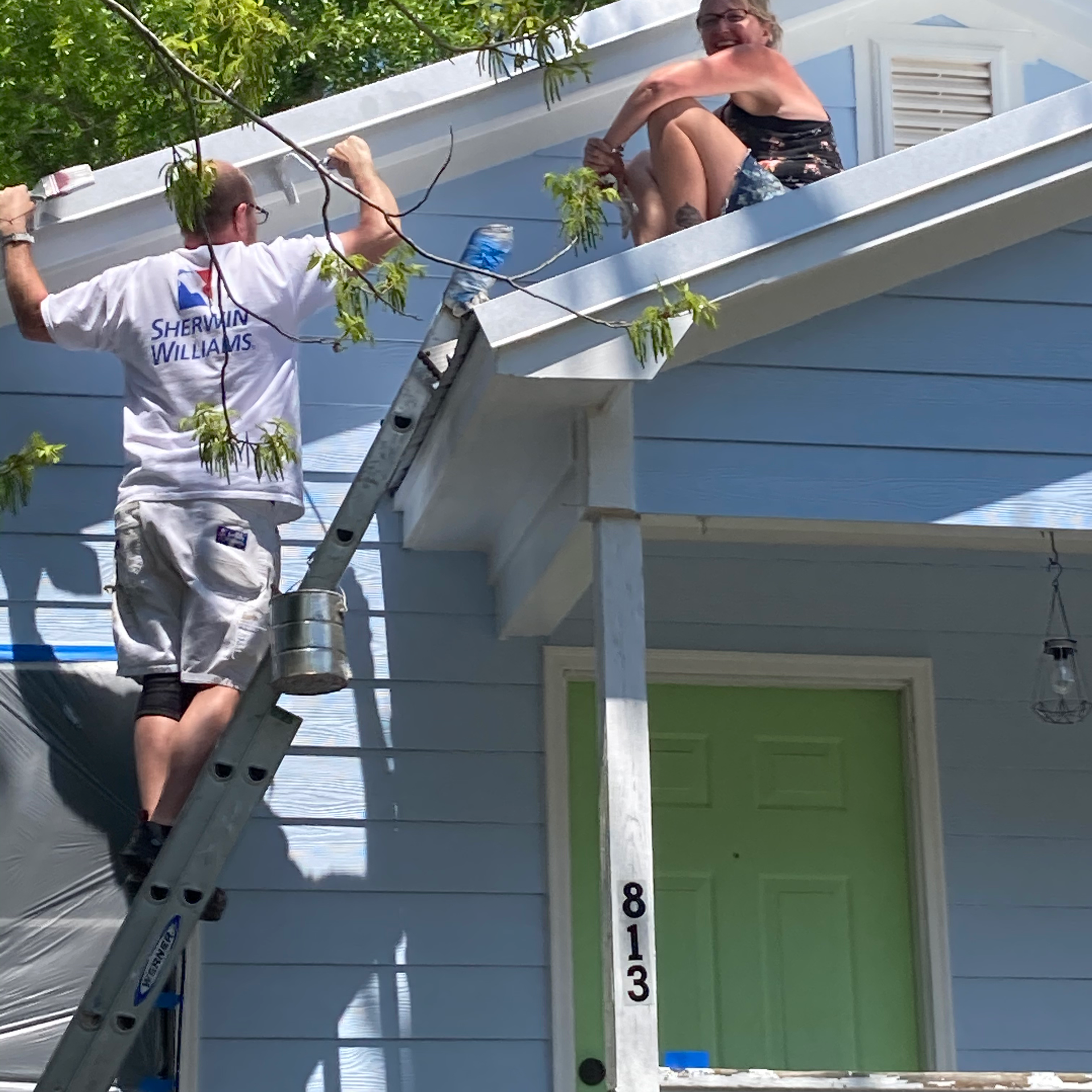 A man on a ladder paints the side of a house