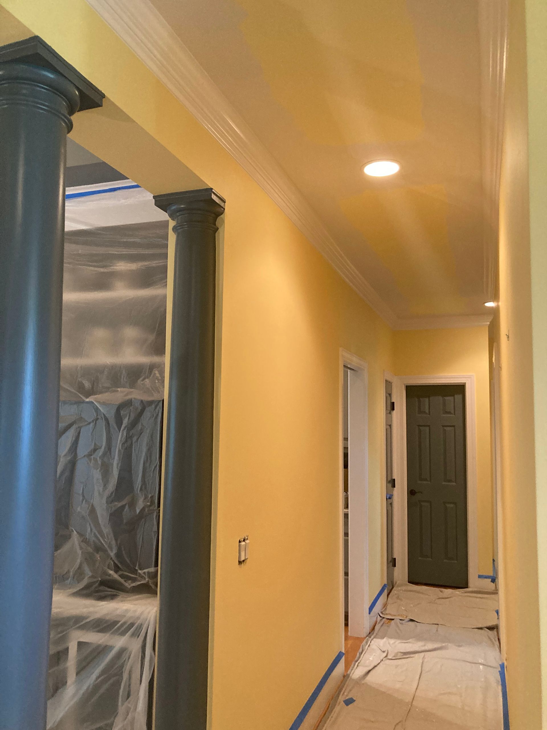 A hallway with yellow walls and columns and a green door