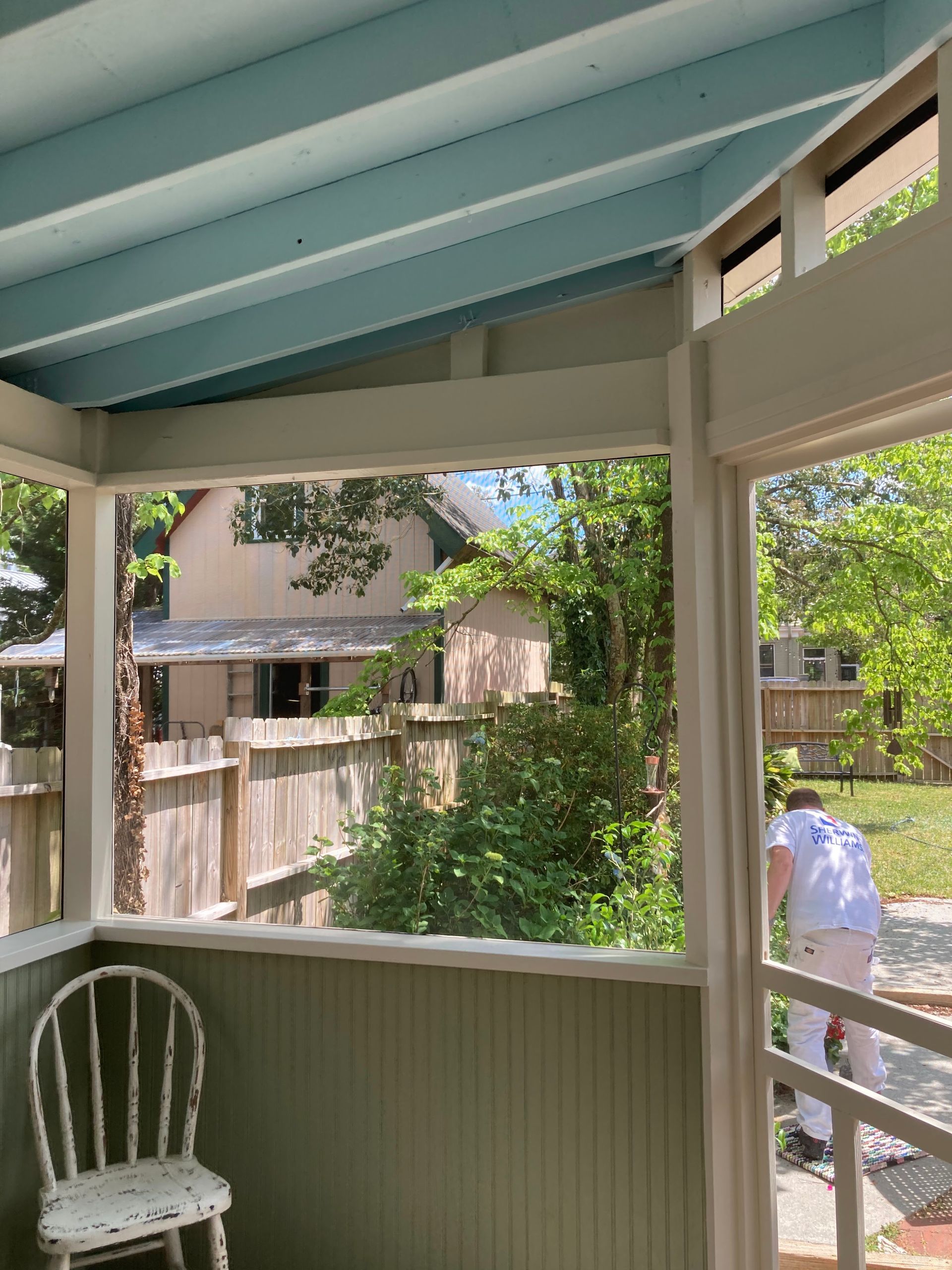 A screened in porch with a chair and a window looking out to a fenced in yard.