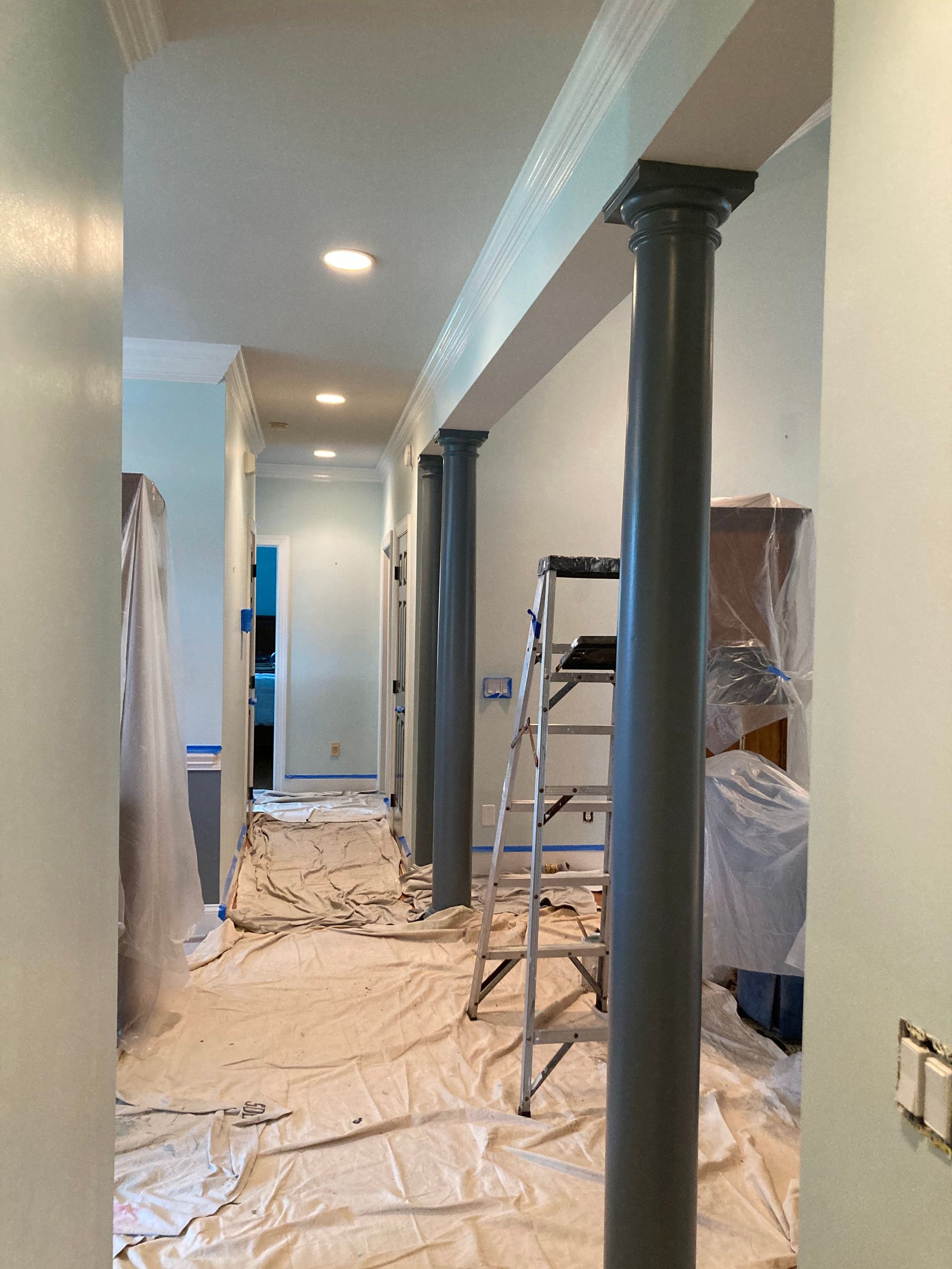 A hallway with columns and a ladder in it is being painted.