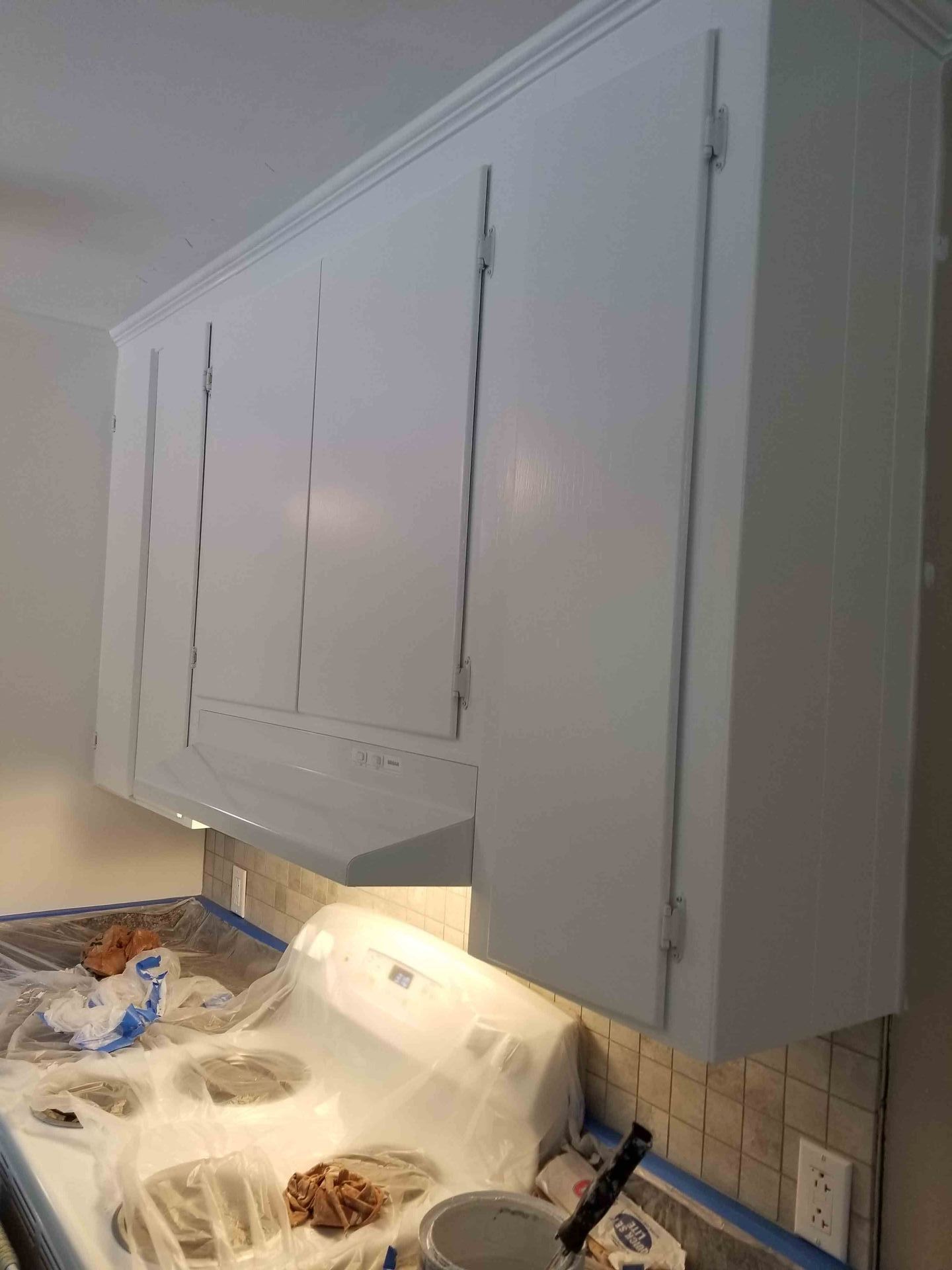 A kitchen with white cabinets and a stove top oven being painted.