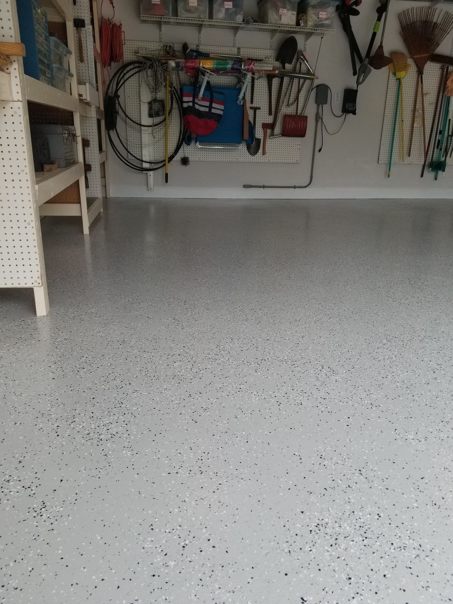 A garage with a white floor and a bunch of tools on the wall.