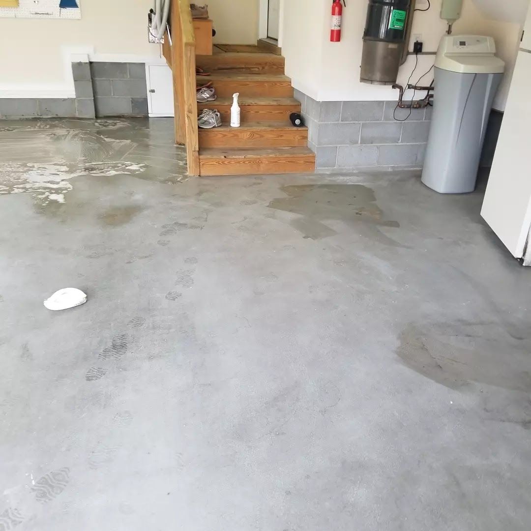 A dirty concrete floor in a garage with stairs and a trash can.