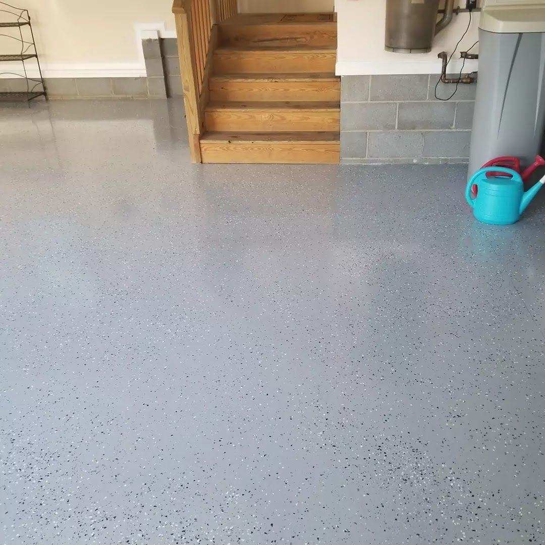 A blue watering can is sitting on the floor of a garage next to stairs.