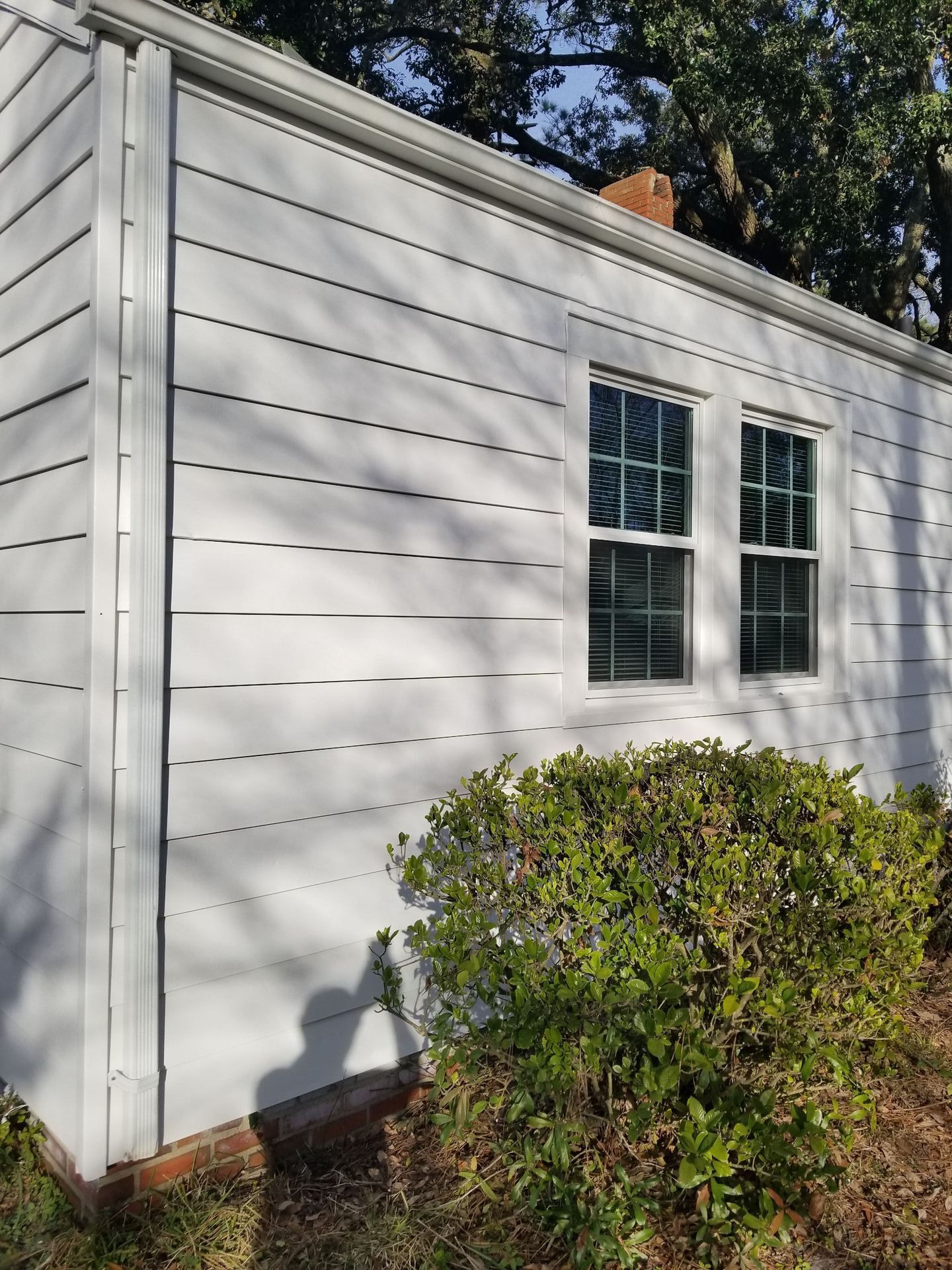 The side of a white house with two windows and a chimney.
