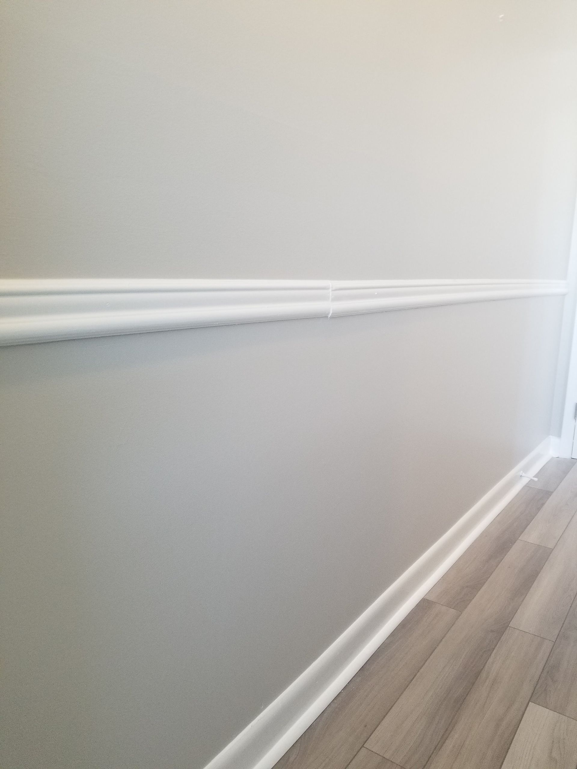A hallway with a gray wall and white trim and a wooden floor.