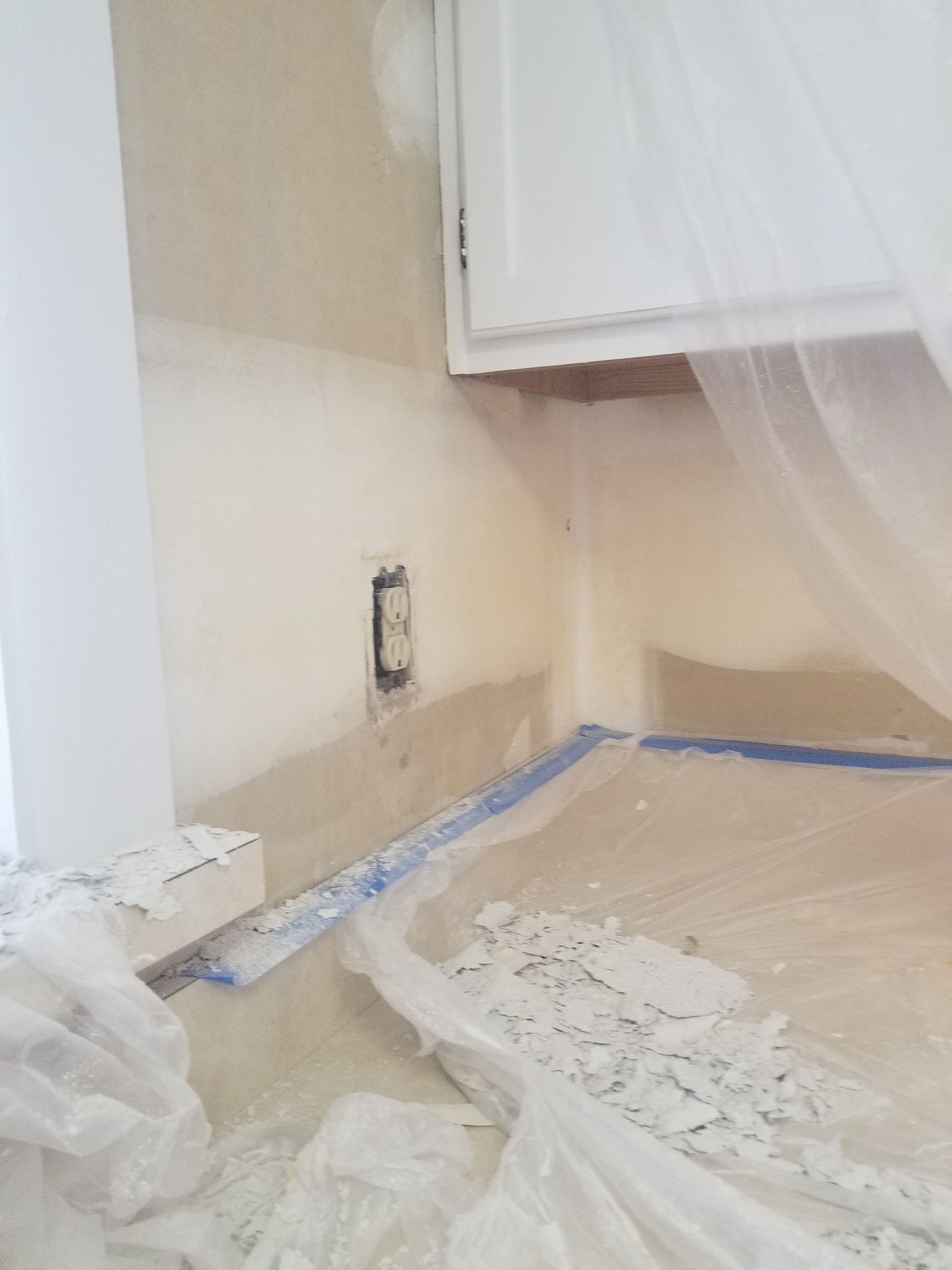 A kitchen is being painted and the floor is covered in plastic.