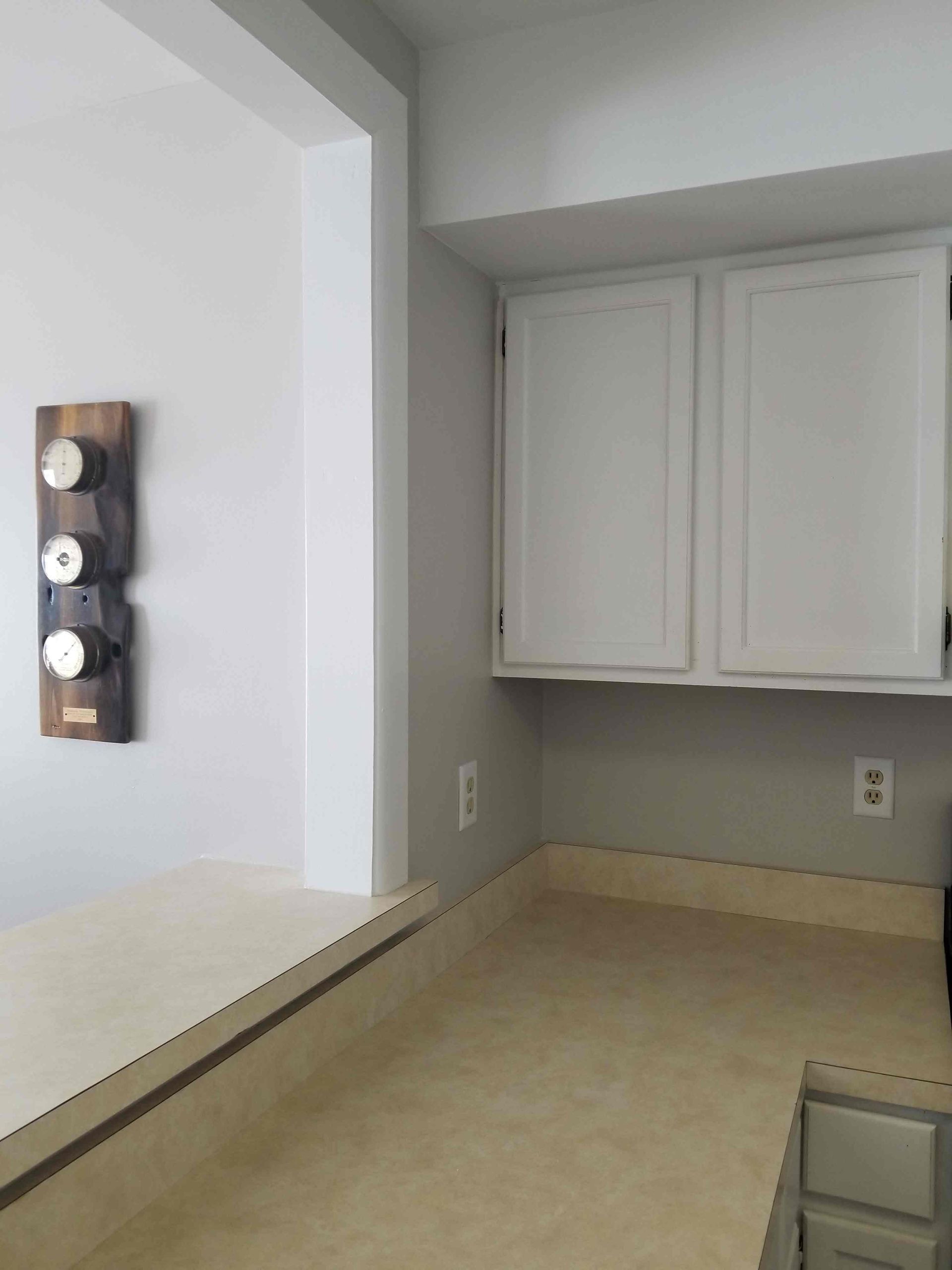 A kitchen with white cabinets and a wooden spice rack on the wall.
