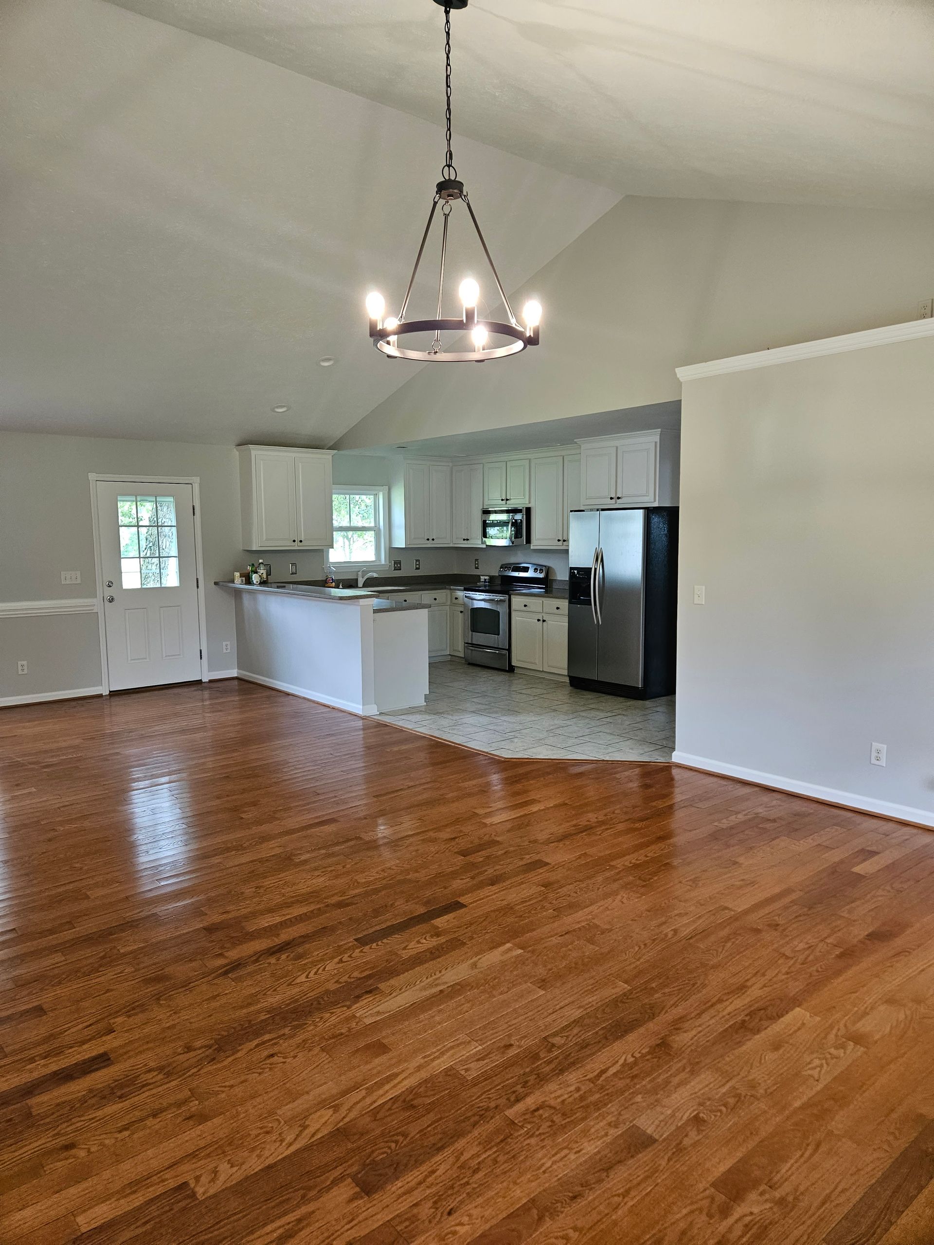 An empty living room with hardwood floors and a kitchen in the background.
