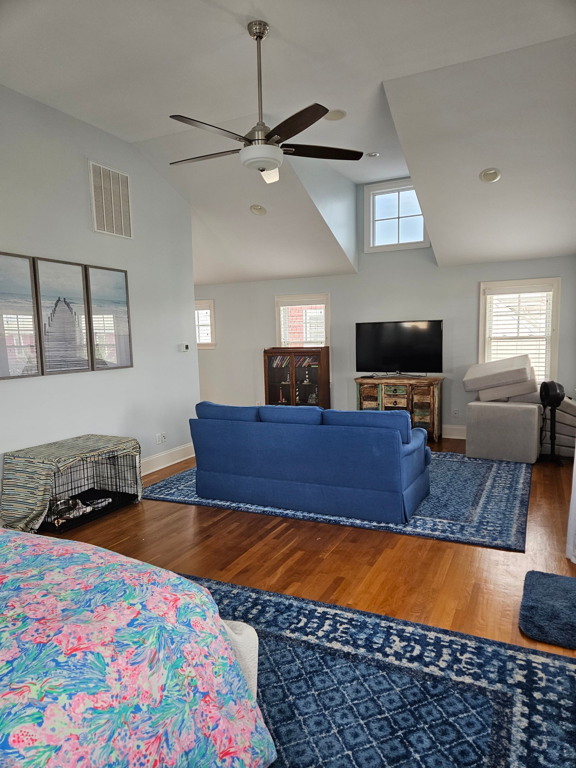 A living room with a blue couch , a flat screen tv , and a ceiling fan.