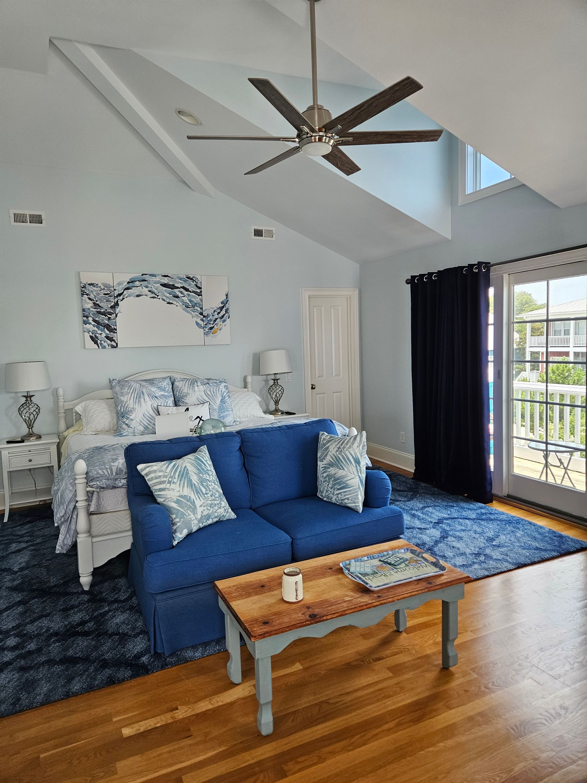 A bedroom with a blue couch , coffee table , and ceiling fan.