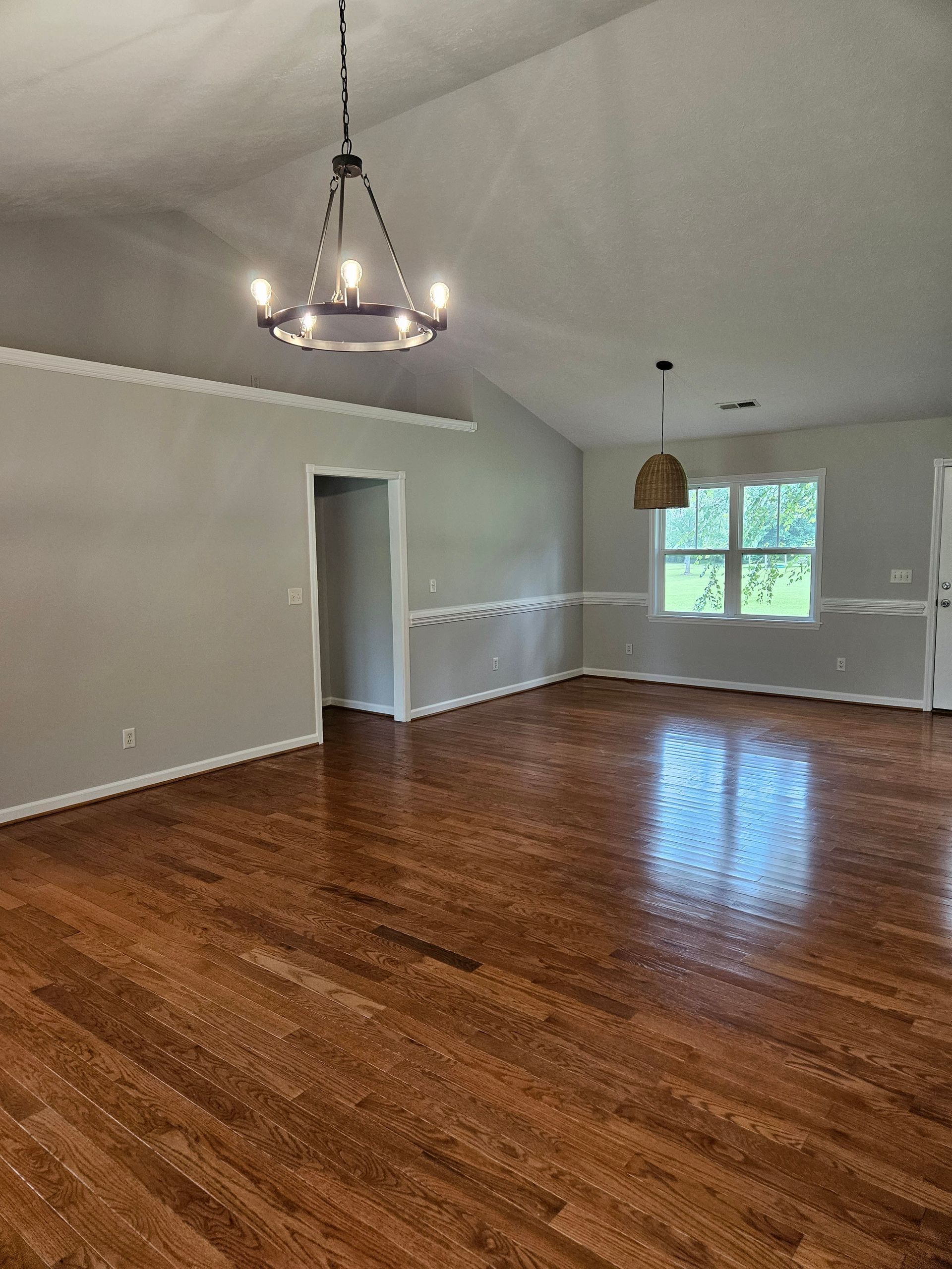 An empty living room with hardwood floors and a chandelier hanging from the ceiling.