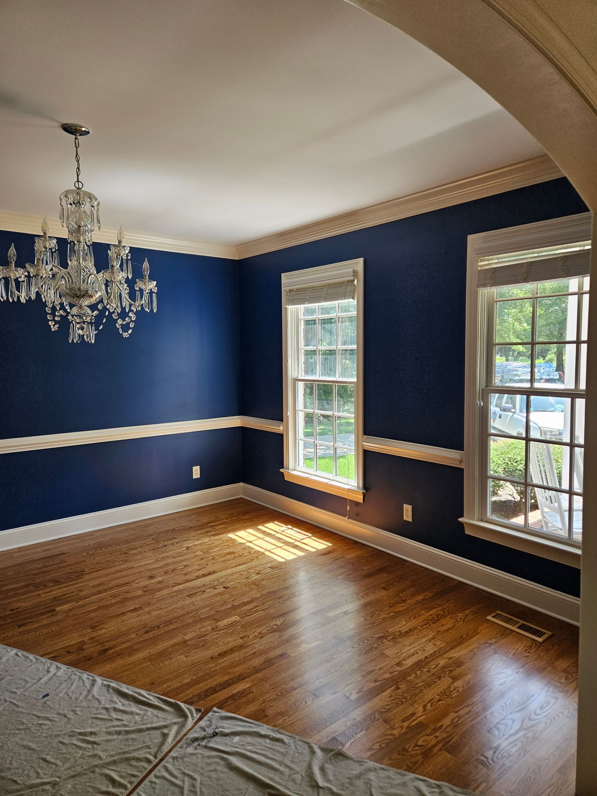 An empty dining room with blue walls and a chandelier hanging from the ceiling.