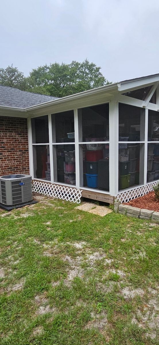 Screened-in porch on a brick house. Air conditioning unit on the side of the house, grass in the foreground. Overcast sky.