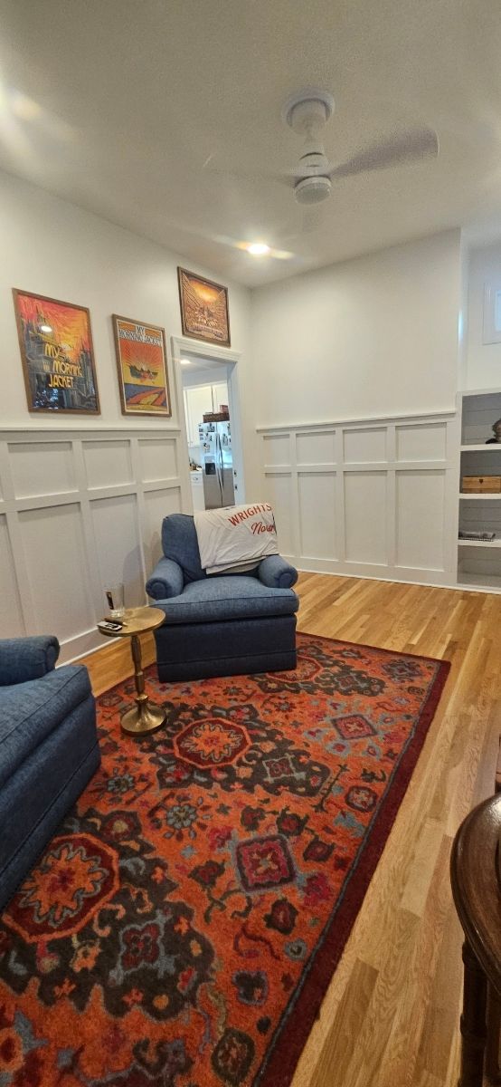 Living room with blue chairs, a patterned rug, and artwork on white paneled walls.