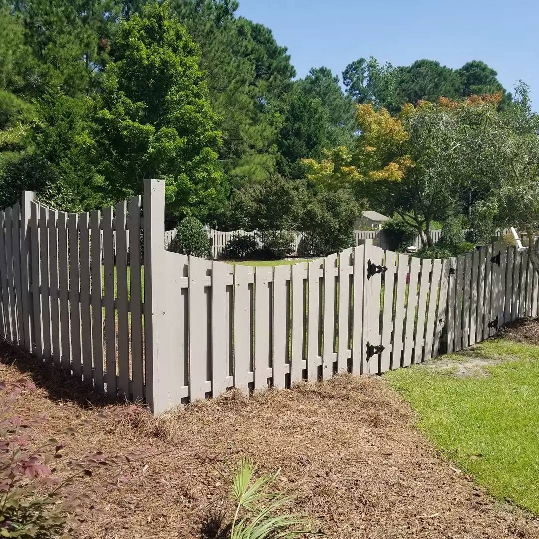 A white picket fence surrounds a lush green field with trees in the background.