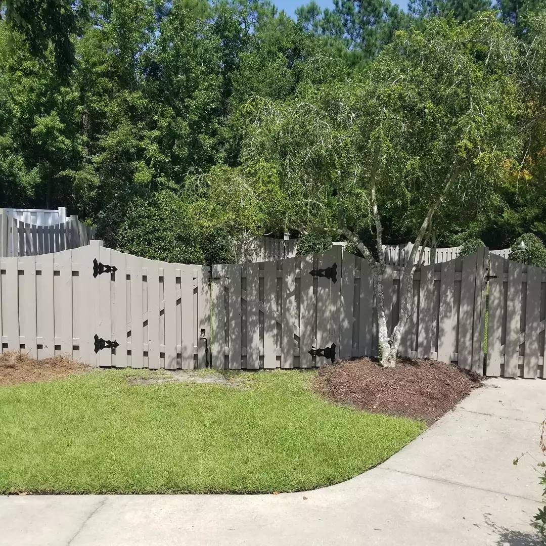 A wooden fence surrounds a lush green lawn next to a sidewalk.