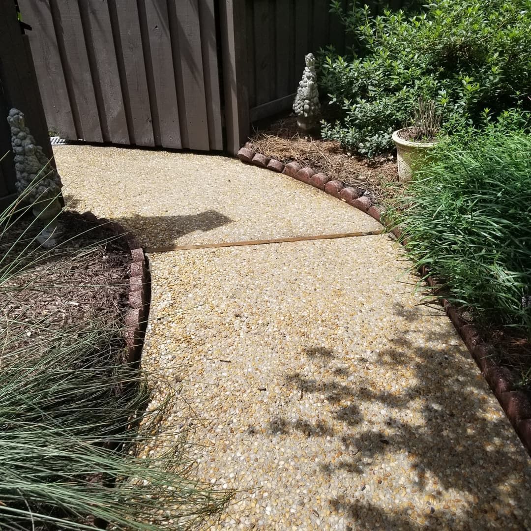 A concrete walkway leading to a wooden gate in a garden.