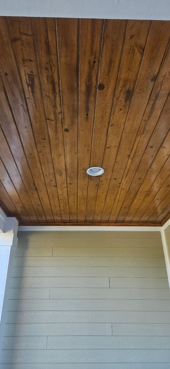 Wooden plank ceiling with a recessed light and light green siding below.