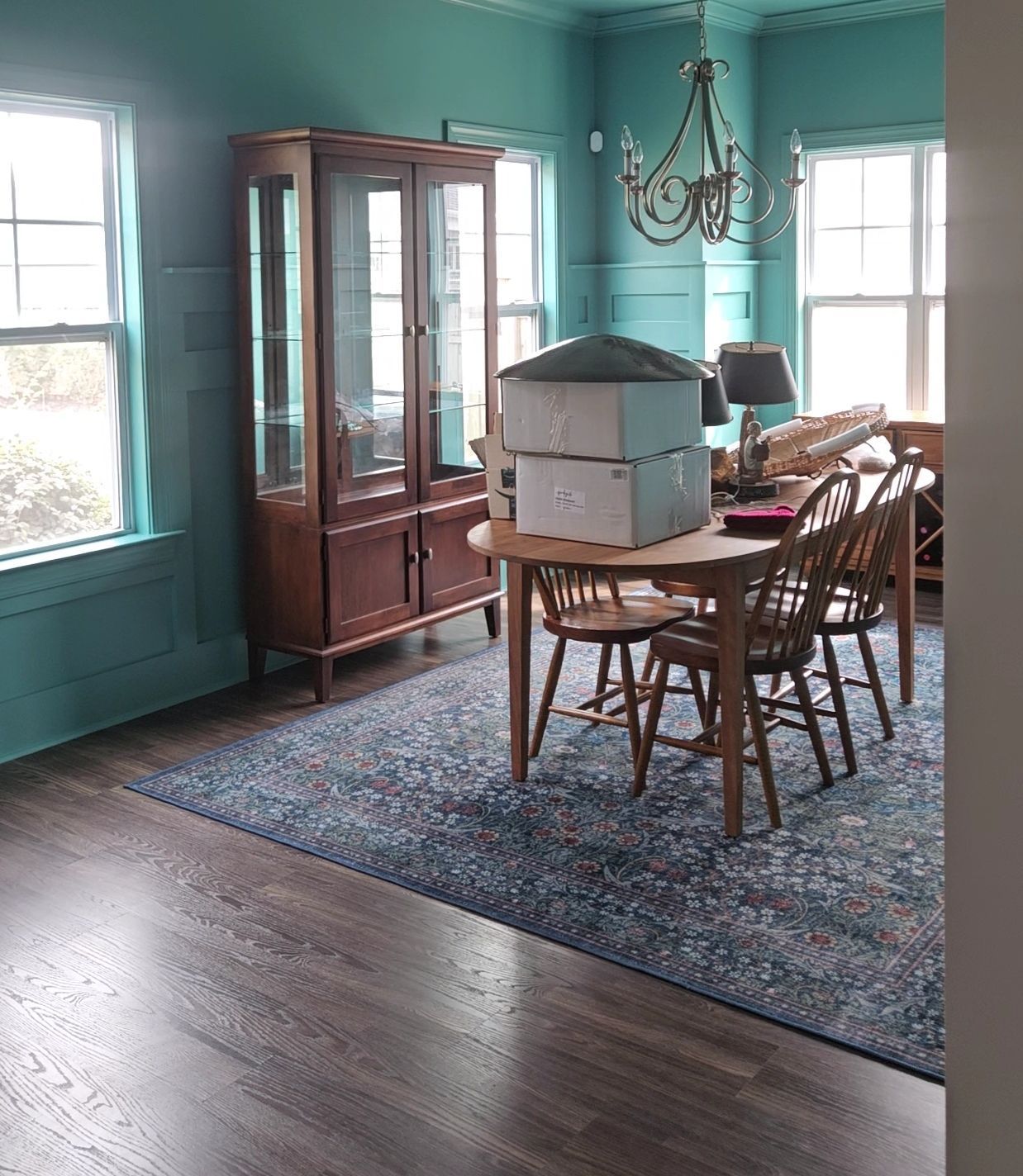 Dining room with teal walls, a dark wood hutch, round wooden table, and blue rug.