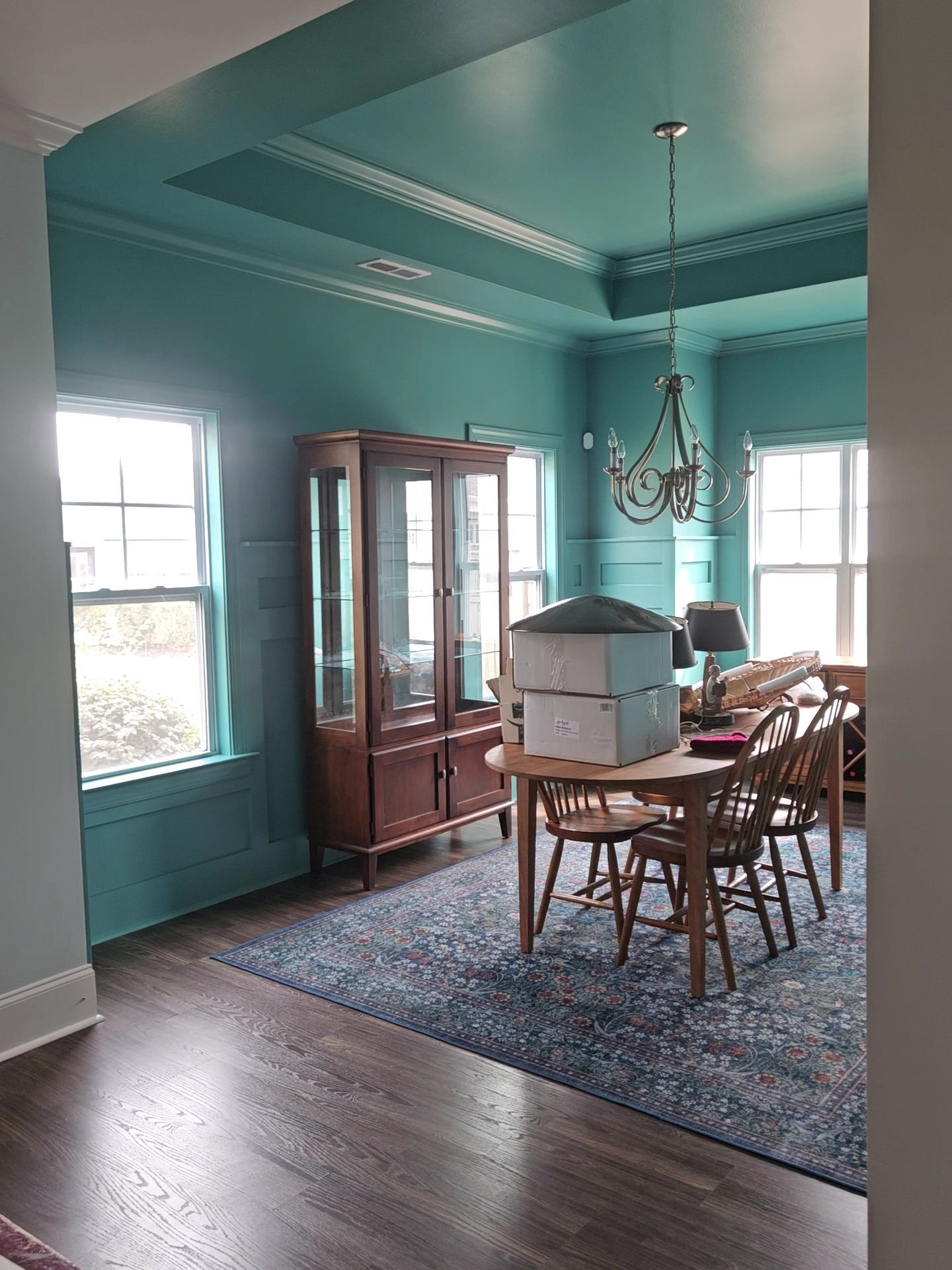 Teal dining room with hutch, table, chairs, rug, and chandelier.
