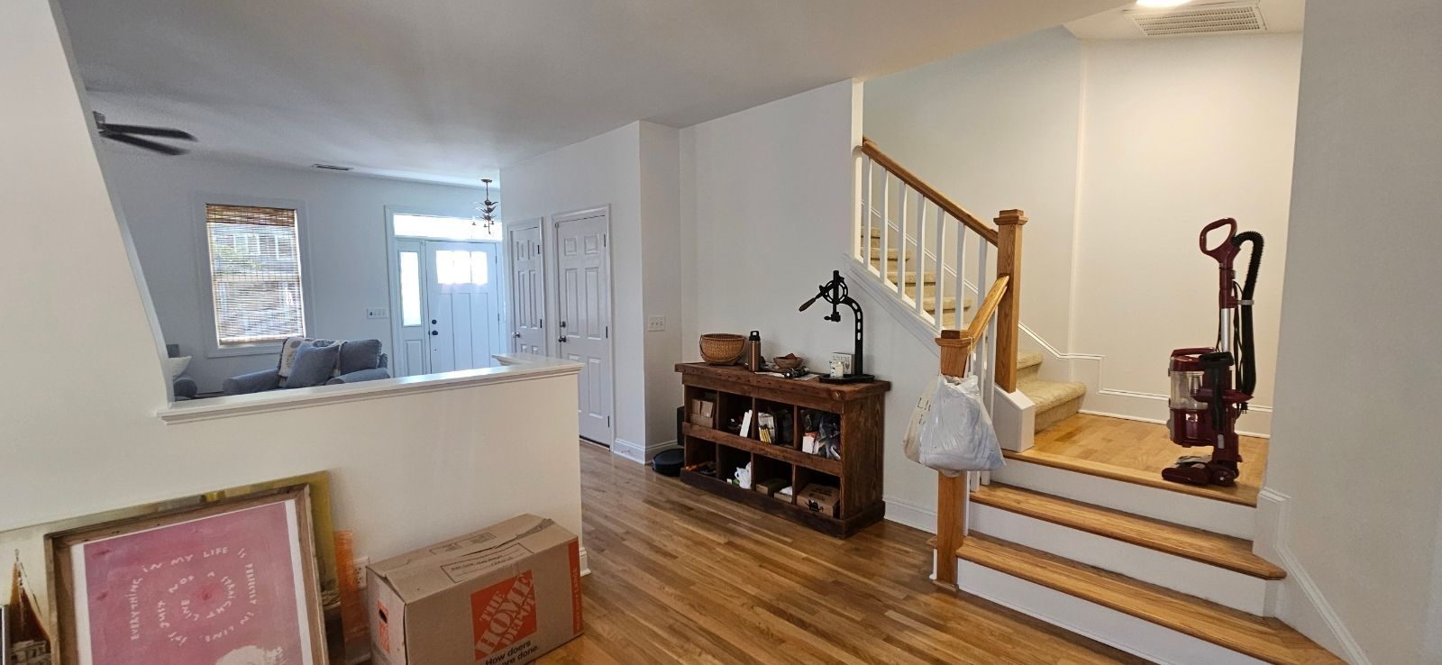 Interior view of a home entrance with hardwood floors and a staircase leading upstairs. A box and art piece are present.
