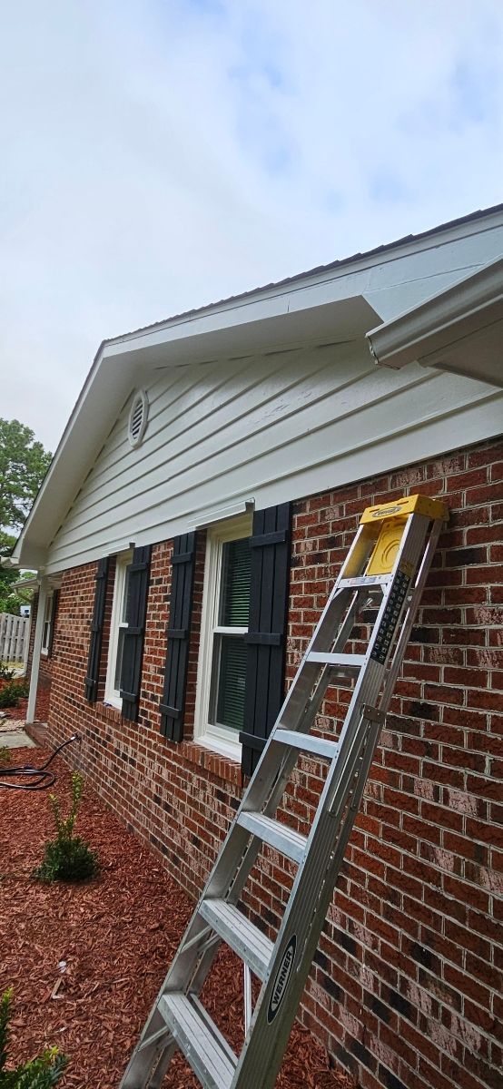 A ladder leaning against a brick house with white siding and black shutters.