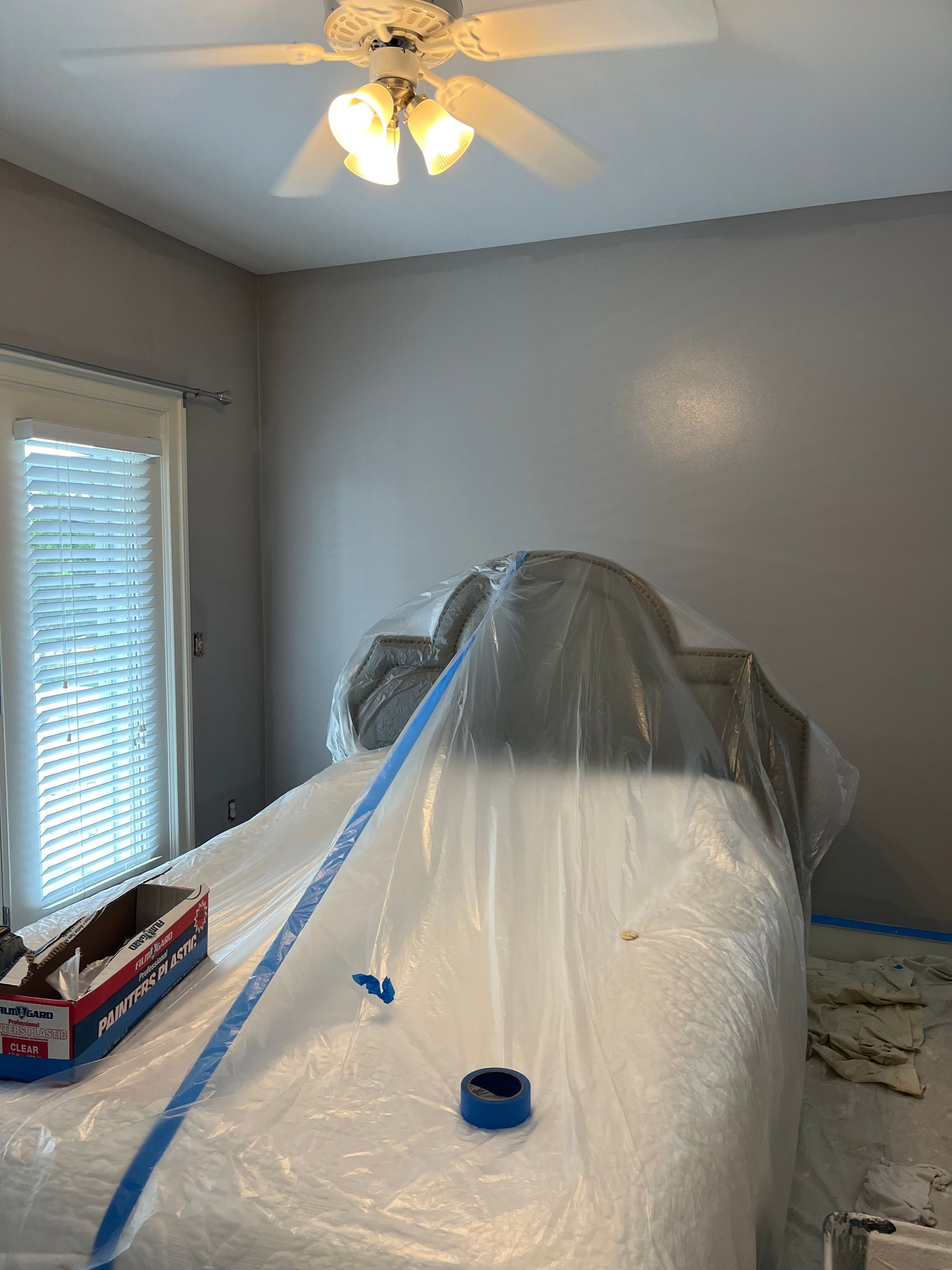 A bedroom with a bed covered in plastic and a ceiling fan.
