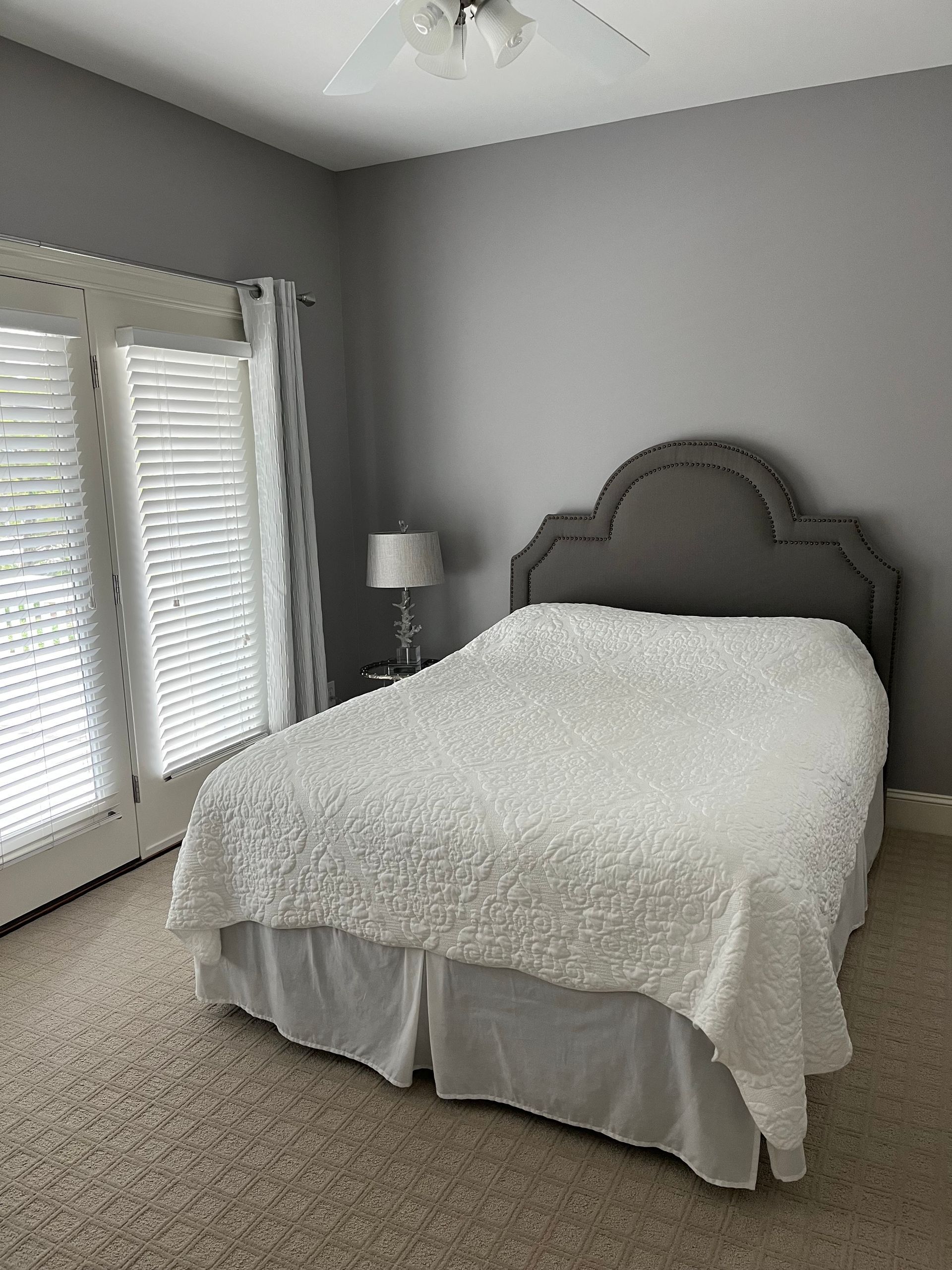 A bedroom with a bed , two windows , a lamp and a ceiling fan.