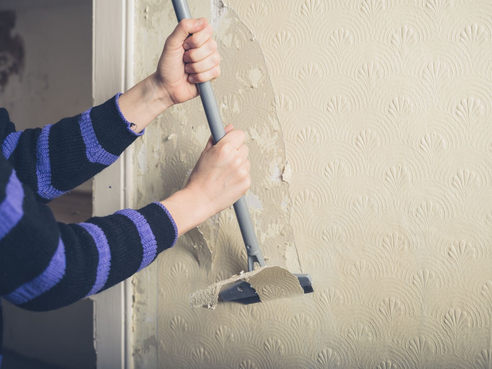 A person is removing wallpaper from a wall with a spatula.