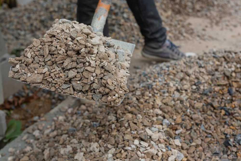 A Person Is Holding A Shovel Filled With Gravel - Order Your Bulk Landscape Supplies in Byron Bay, NSW