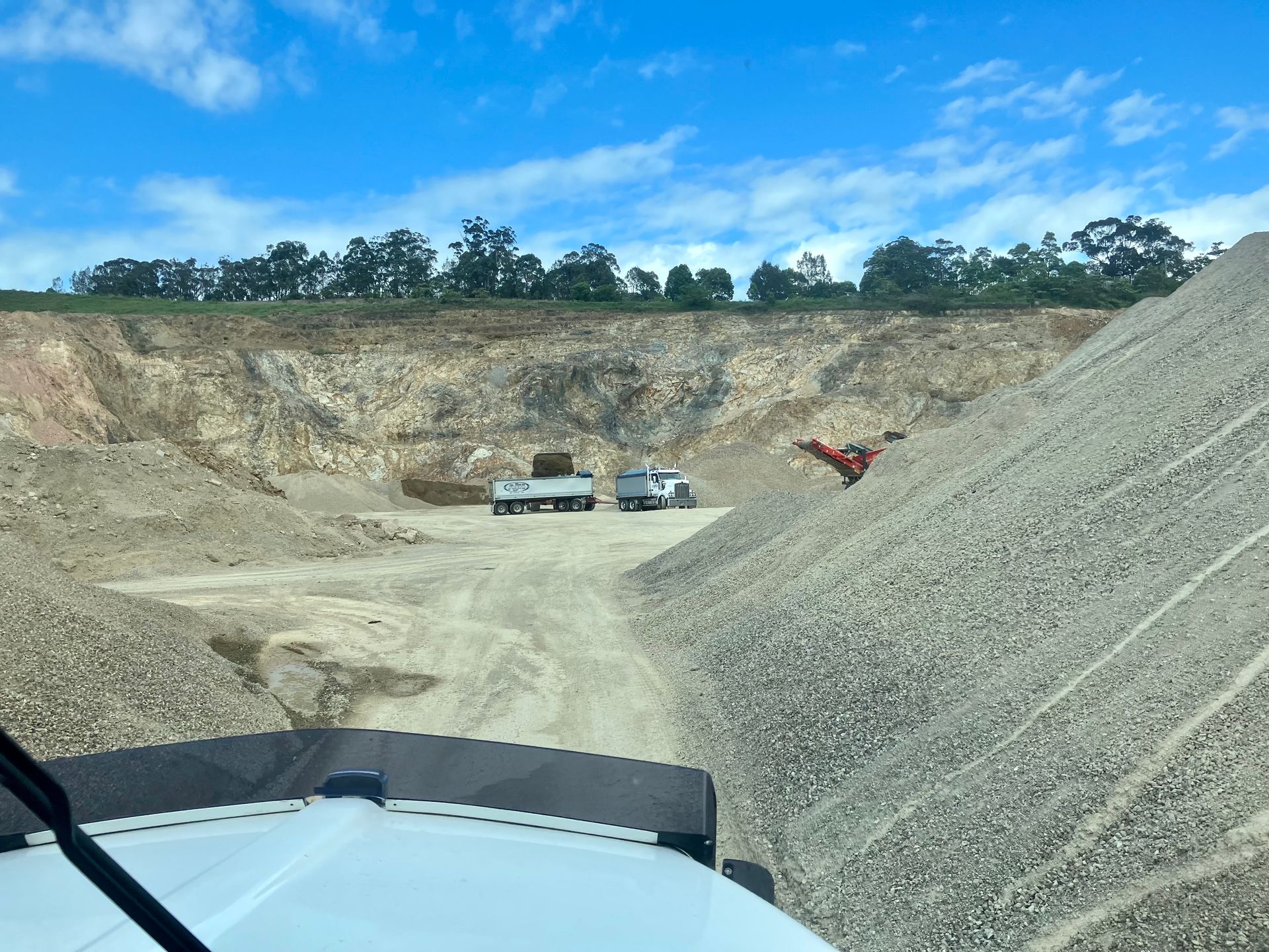 A Truck is Driving Down a Dirt Road Next to a Large Pile of Gravel  — Andrew Johnston Haulage In Ewingsdale, NSW
