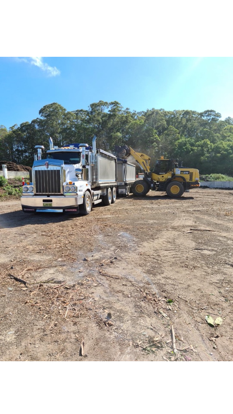 A Dump Truck is Driving Down a Dirt Road Next to a Bulldozer — Andrew Johnston Haulage In Ewingsdale, NSW