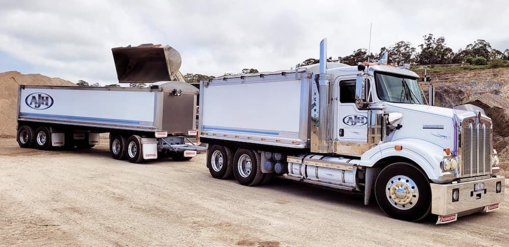 A Dump Truck With a Trailer Attached to It is Parked on a Dirt Road  — Andrew Johnston Haulage In Ewingsdale, NSW