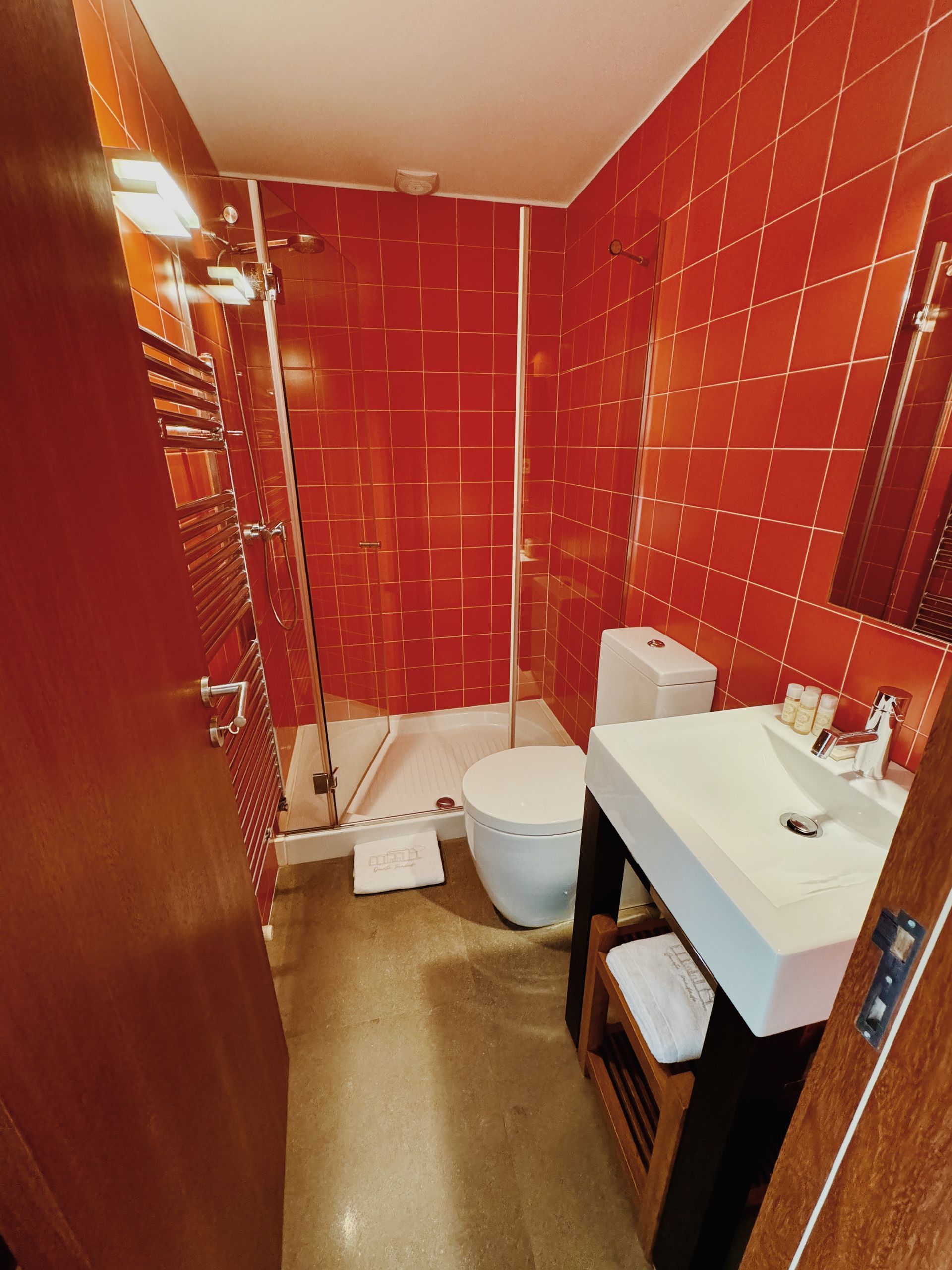 Um banheiro com azulejos vermelhos, vaso sanitário, pia e chuveiro.