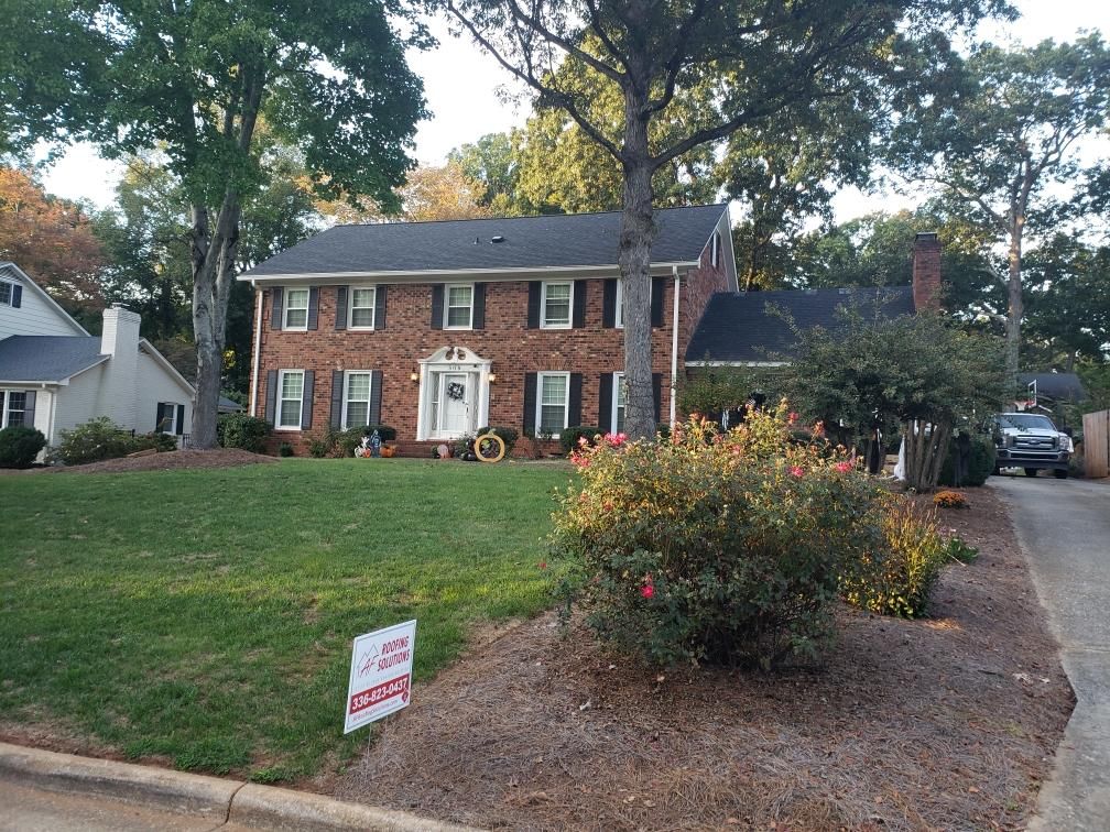 Two-story brick house with a front lawn, driveway, and shrubs in a suburban neighborhood.