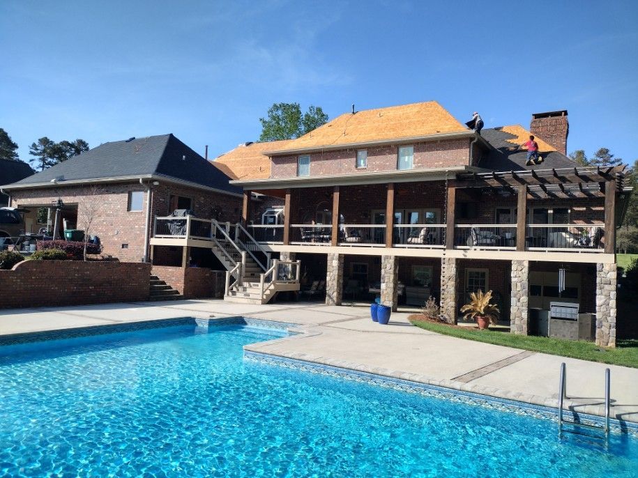 Backyard with a blue swimming pool and a brick house with a wooden deck under a sunny sky