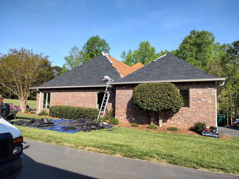 Brick suburban house with dark gray roofs, front lawn, and tree-lined street on a sunny day