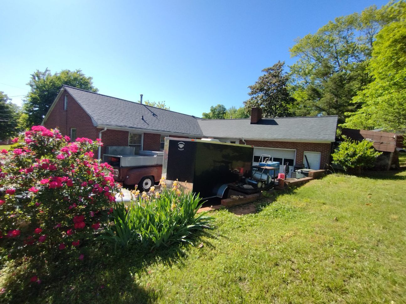 Suburban house with carport, red brick walls, and a lush green lawn under a bright blue sky
