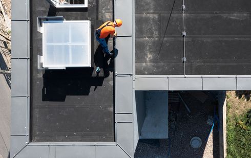 Worker in orange vest on a rooftop beside a white skylight.